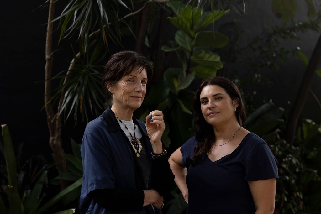 older woman and younger woman standing in front of greenery