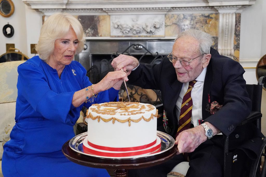 Queen Camilla and an old man cutting into a cake with white icing