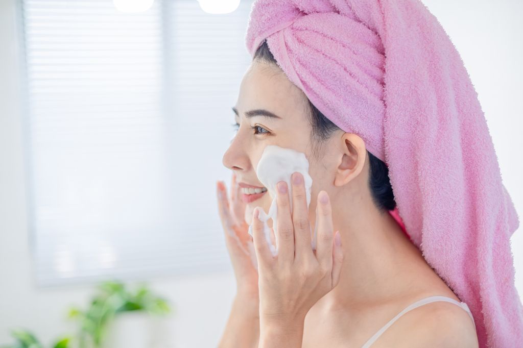 woman with towel on head is cleaning her face by facial cleanser in the bathroom