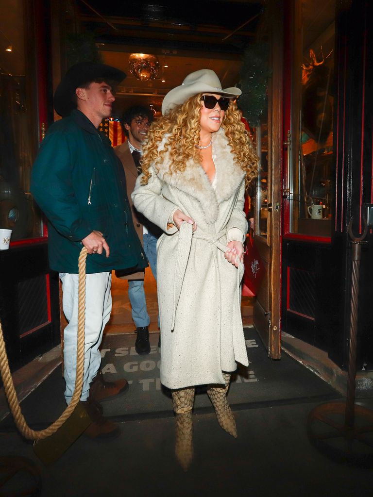 Mariah Carey in Aspen leaving a shop wearing a beige cowboy hat and matching coat, plus patent leather boots and black sunglasses.