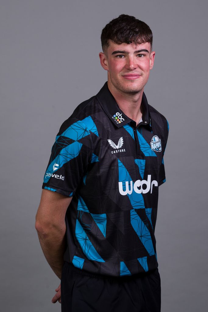 Jish Baker in a black and blue uniform in front of a grey background