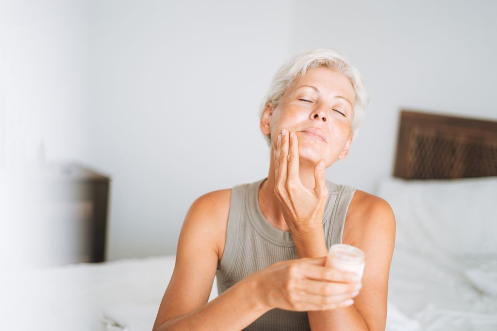 Beautiful woman with short hair applies cream to her face at home, morning skincare routine