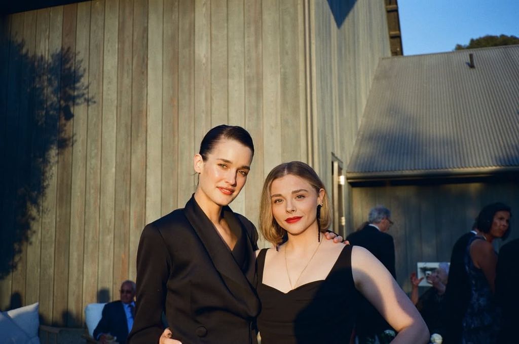 Chloe Moretz in black dress posing with Kate Harrison in black suit at a wedding