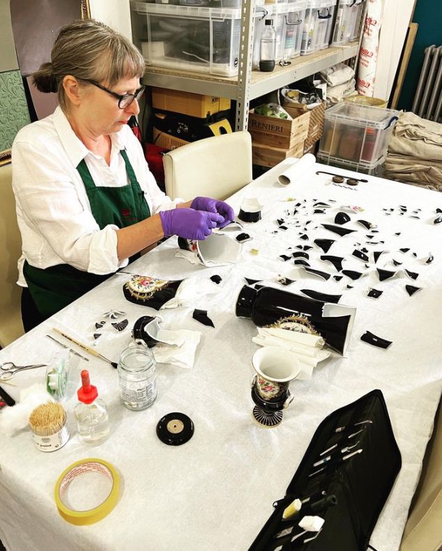 A restorer working on a shattered black vase