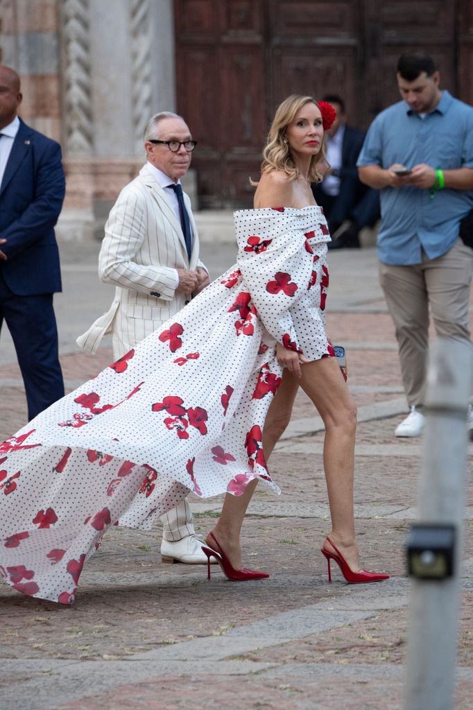 Dee Ocleppo Hilfiger wears an off-shoulder short dress with a polka-dot and red floral train, accessorised with red heels and a flower in her hair.