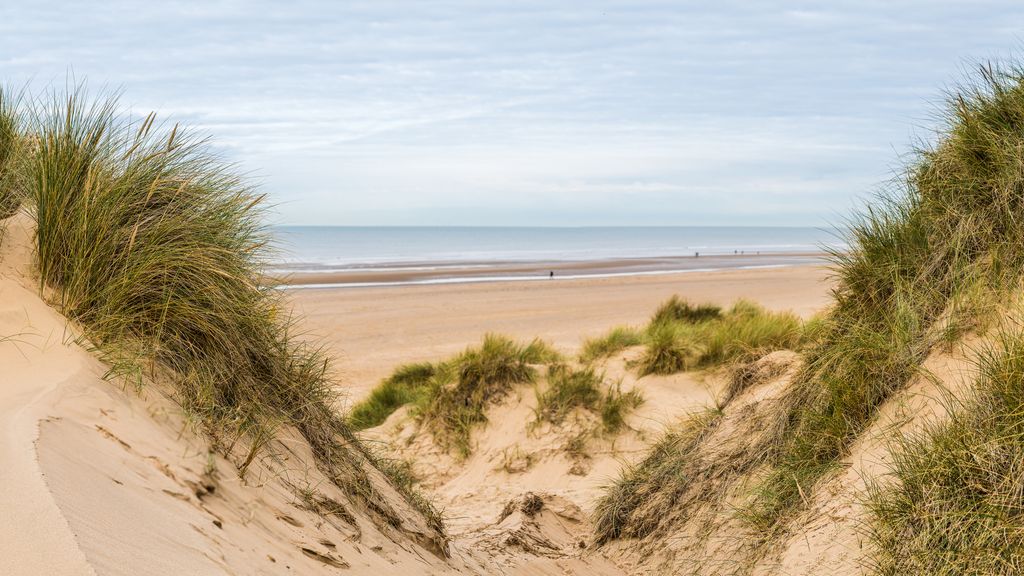 Un panorama multi-image capturé entre deux sommets sur les dunes de sable en regardant les gens marchant le long de Formby Beach près de Liverpool.