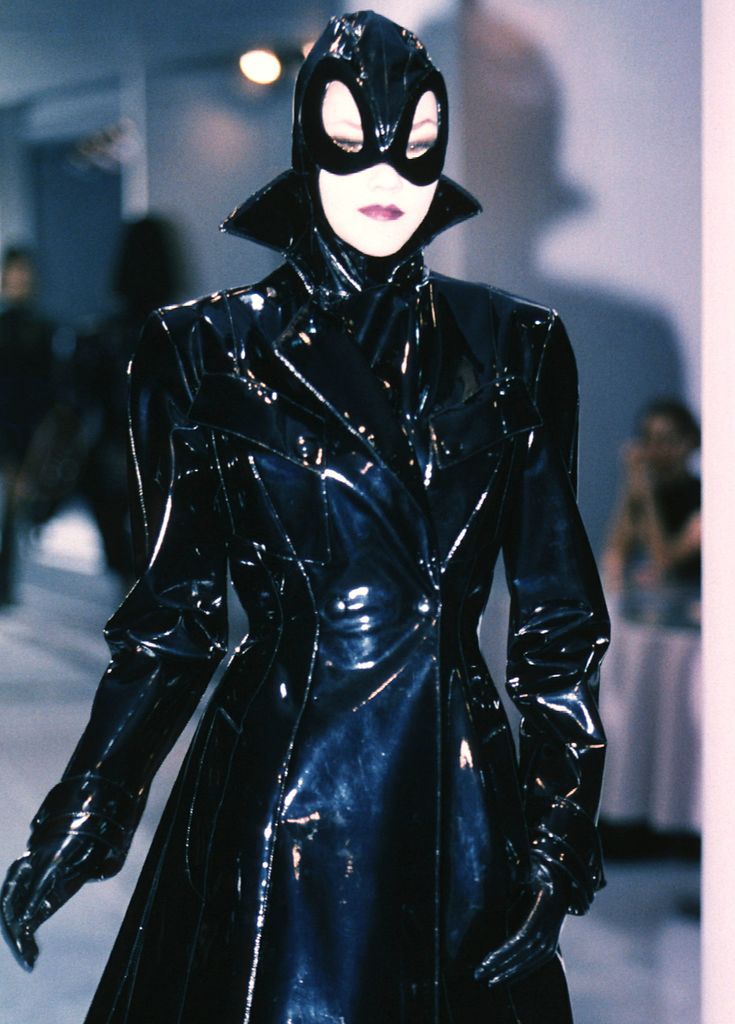 Thierry Mugler AW 1996 collection - a model wears a latex coat, gloves and mask as she walks down the runway