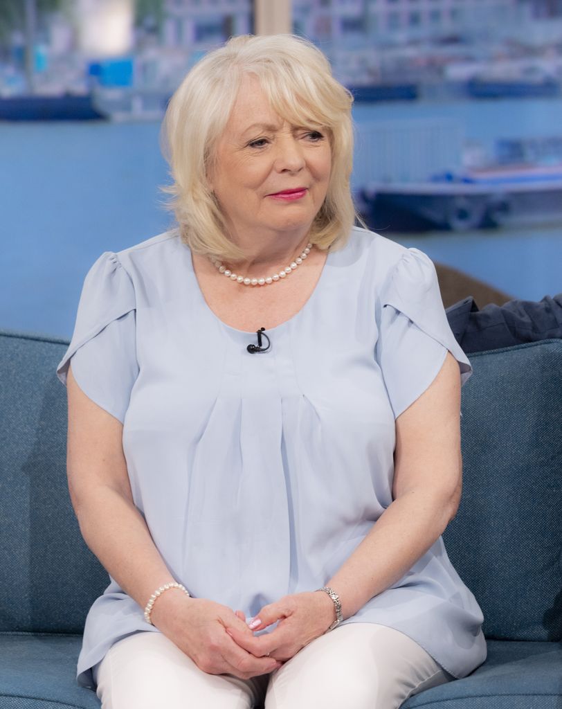 Alison Steadman looking sad in a blue dress and pearl necklace