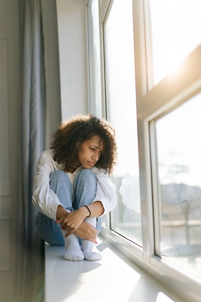 sad and lonely woman with emotional pain sitting in window.