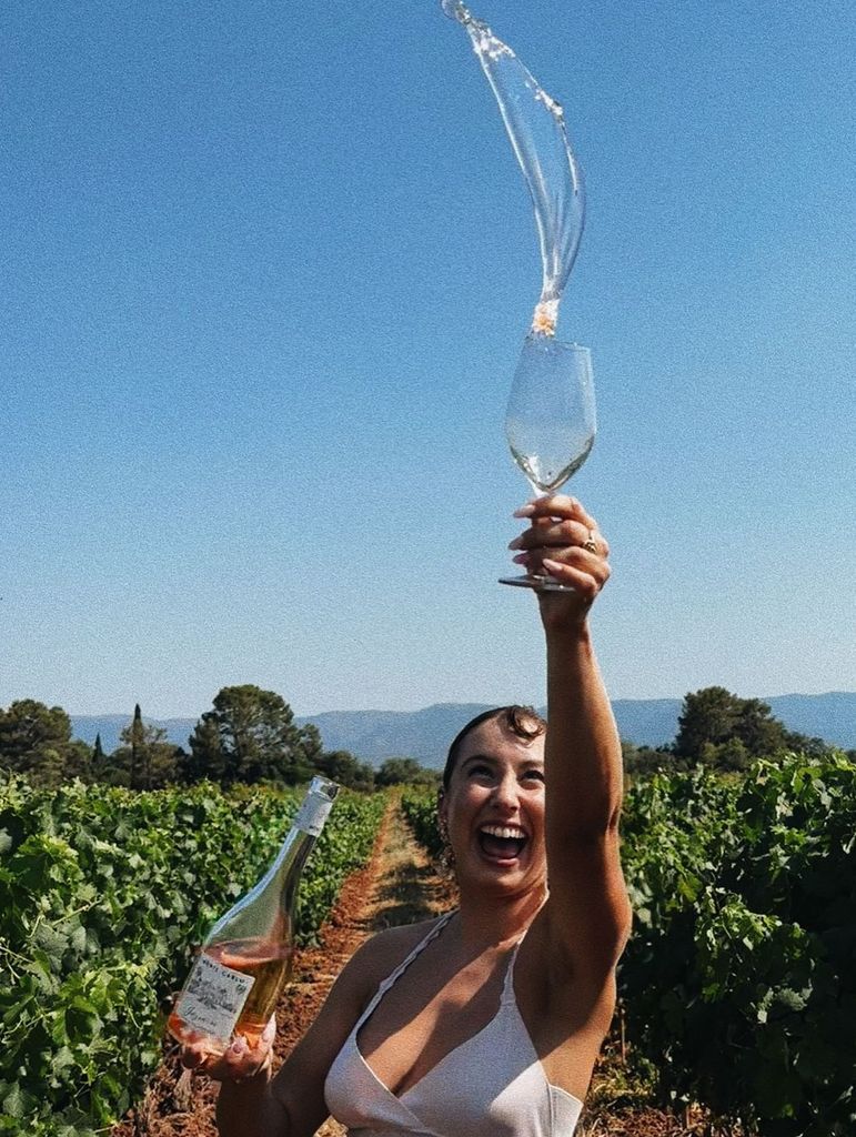Jazmin Grace Grimaldi standing in a vineyard throwing wine in the air 