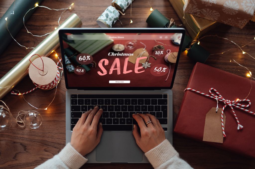 Female hand using laptop while wrapping Christmas gifts.