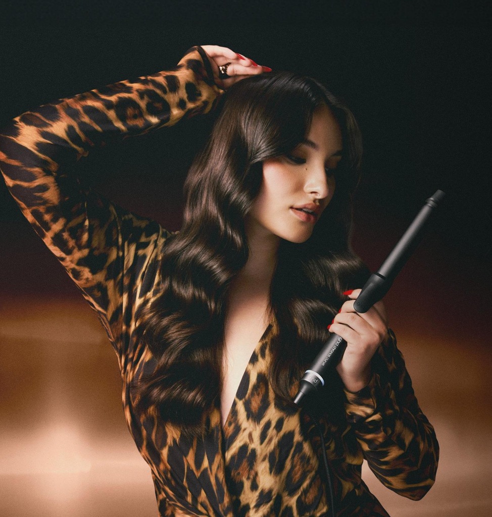 Model with long, dark curly hair holding ghd curler