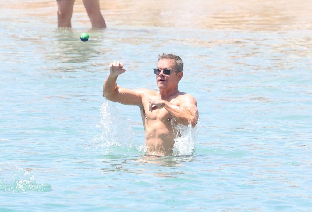 Matt Damon catches a ball thrown to him as he stands in the ocean 