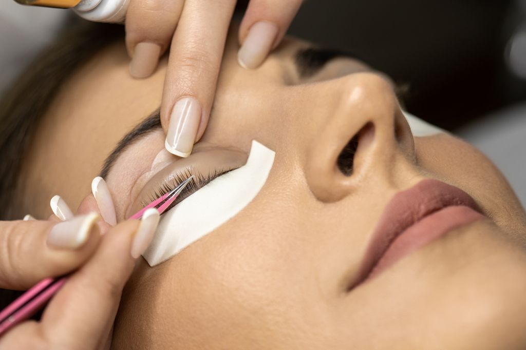 Beautiful young woman with beautiful clean skin having a lash lift treatment. She is laying on the bed, her eyes are closed and the beautician is doing the treatment.