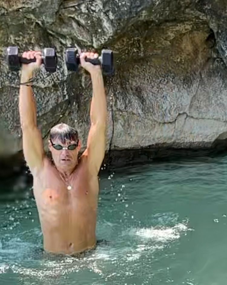 ryan seacrest in the water holding up dumbbells and wearing goggles