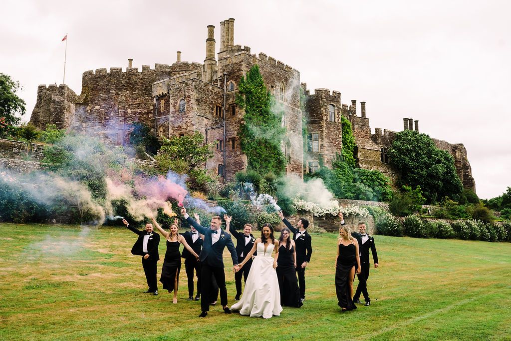 Berkeley Castle with wedding guests in black letting off coloured smoke bombs