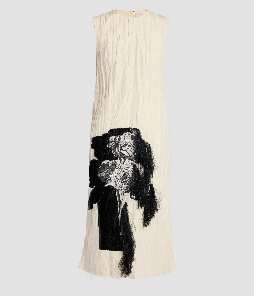 A close-up of the white Erdem dress showcases intricate black embroidered florals and textured embellishments cascading down one side. The sleeveless design and fluid silhouette highlight its timeless elegance and avant-garde appeal.