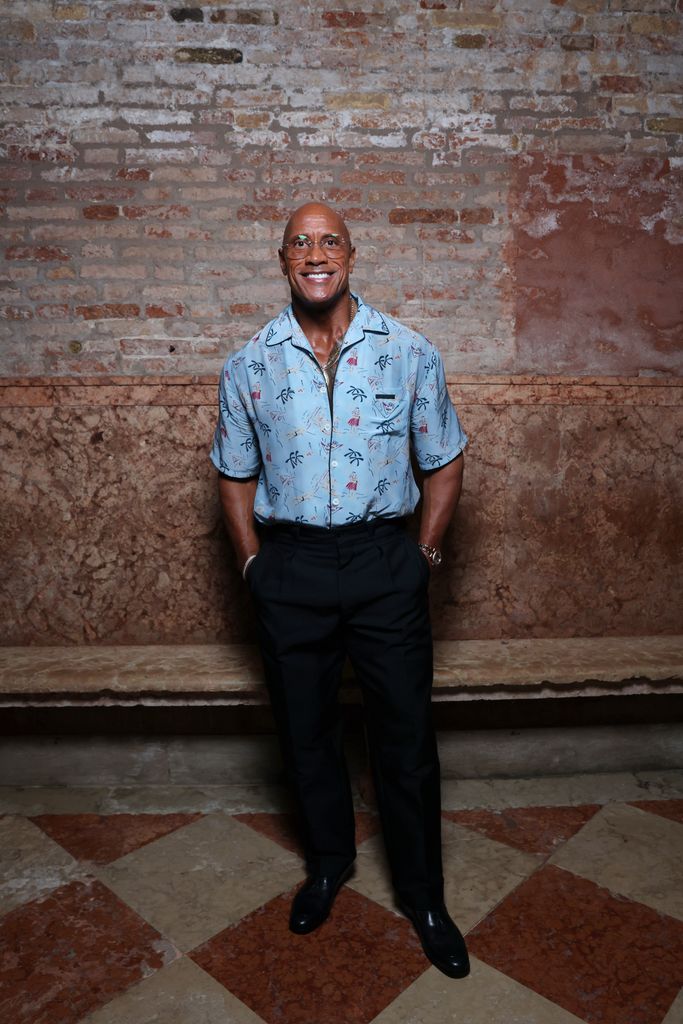 The Rock smiling wearing a blue shirt, looking slim