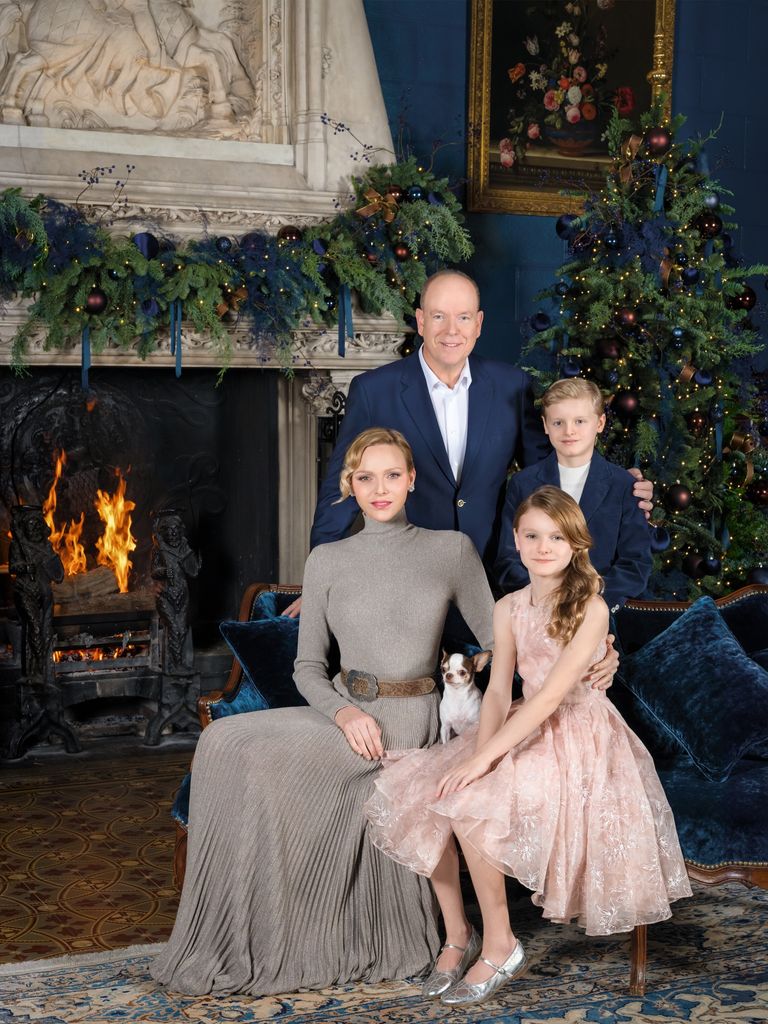 prince albert, princess charlene and two children pose in front of christmas tree and fireplace