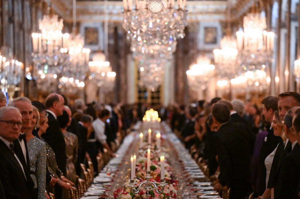 Candles and chandeliers illuminate the room as royals attend a state banquet at the Palace of Versailles