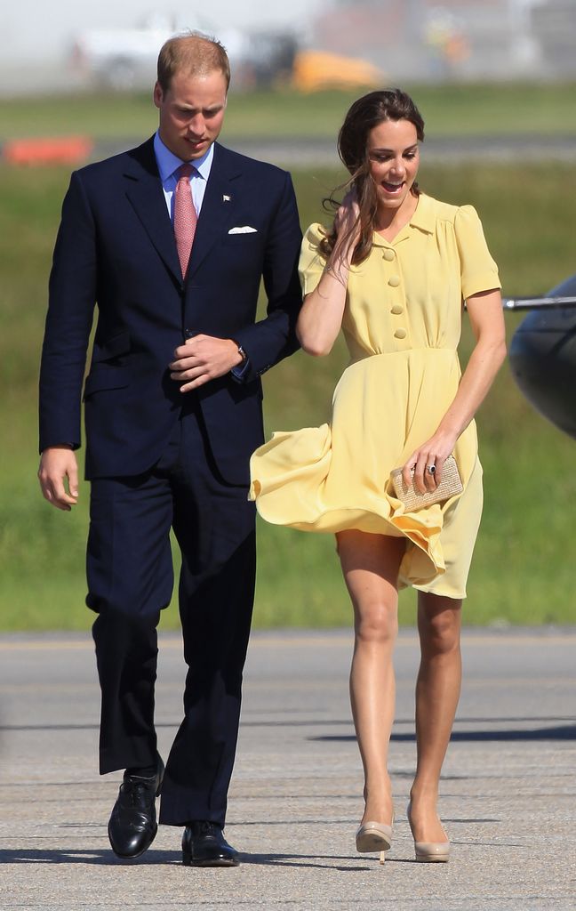 Prince William in a suit with Kate Middleton holding down her yellow dress in the wind