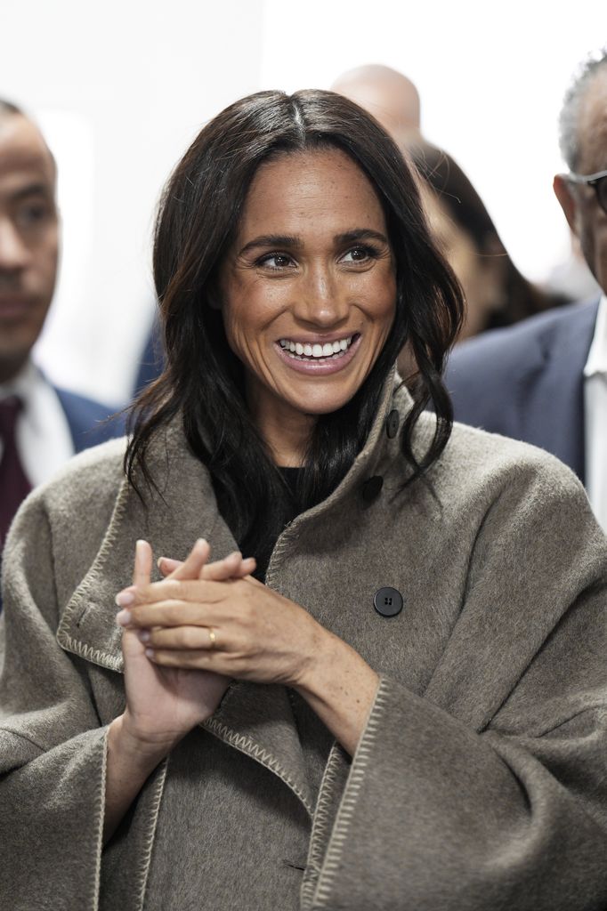 Meghan souriante dans un manteau taupe