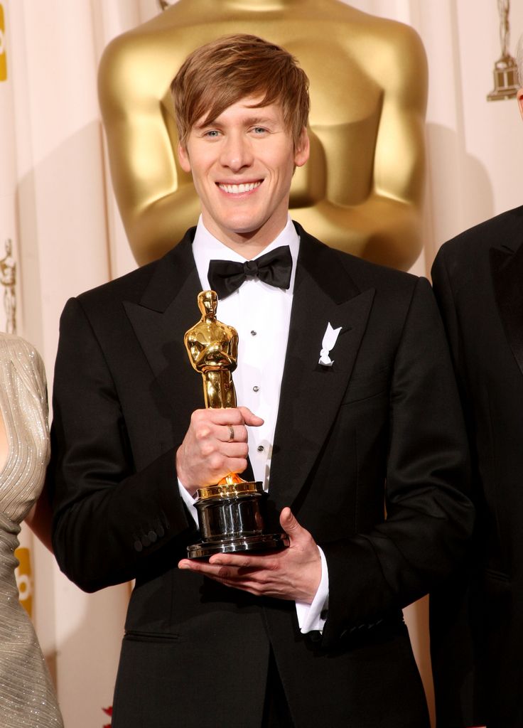 Dustin Lance Blakc in a tuxedo holding an Oscar award