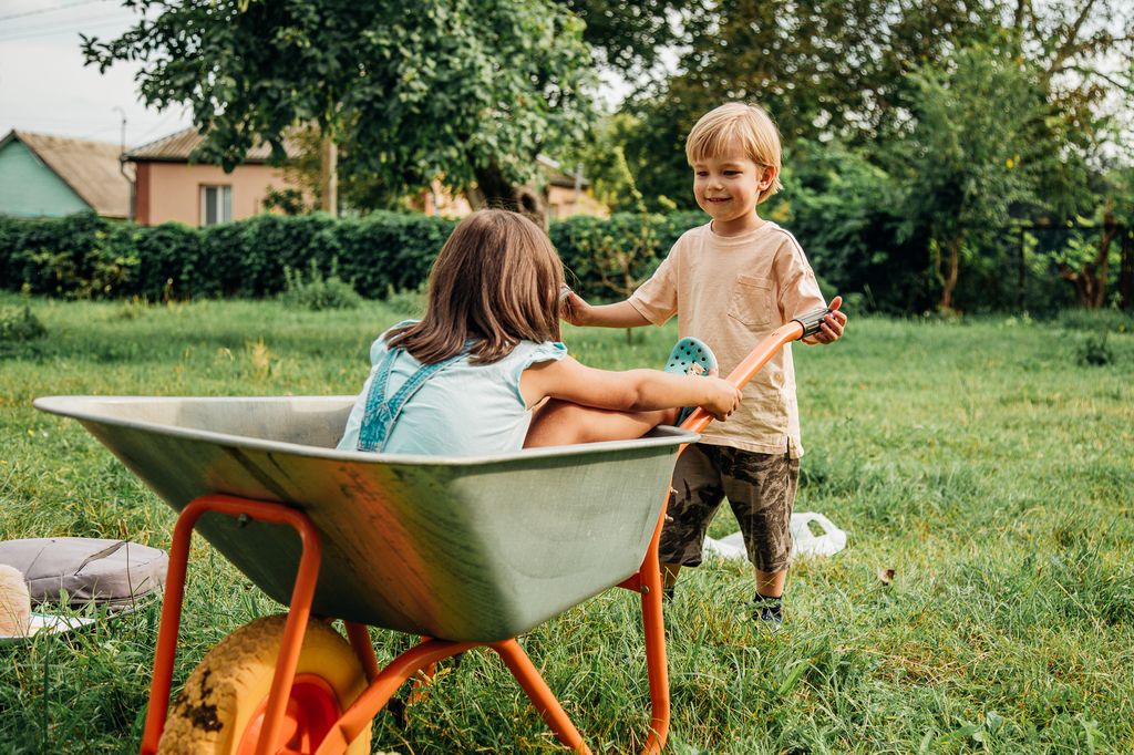 Happy children playing with a wheelbarrow in summer