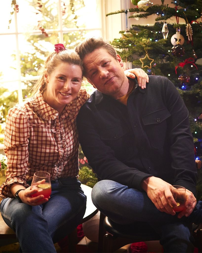 Jamie Oliver holding a drink with his wife Jools in front of a Christmas tree