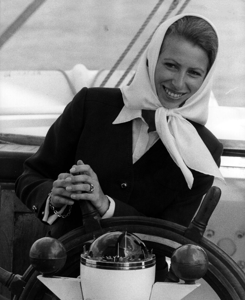 Princess Anne wearing blazer and headscarf at the helm of a yacht