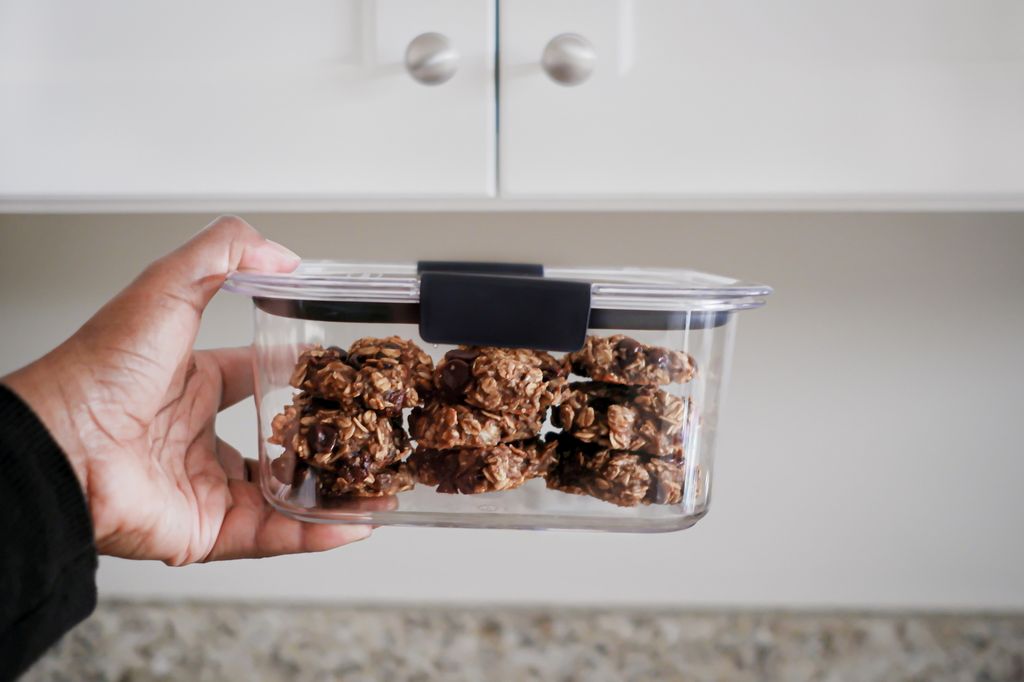 Close-up of unrecognizable black woman storing a small batch of homemade banana oatmeal chocolate chip cookies in an airtight container