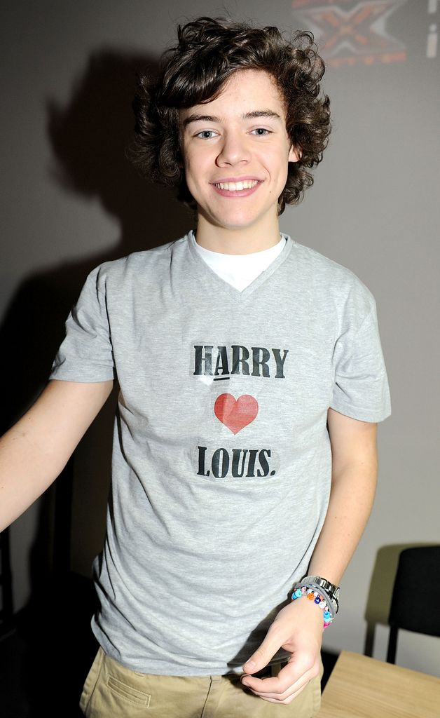 A 17-year-old Harry Styles smiles while wearing a grey "Harry Heart Louis" T-shirt.