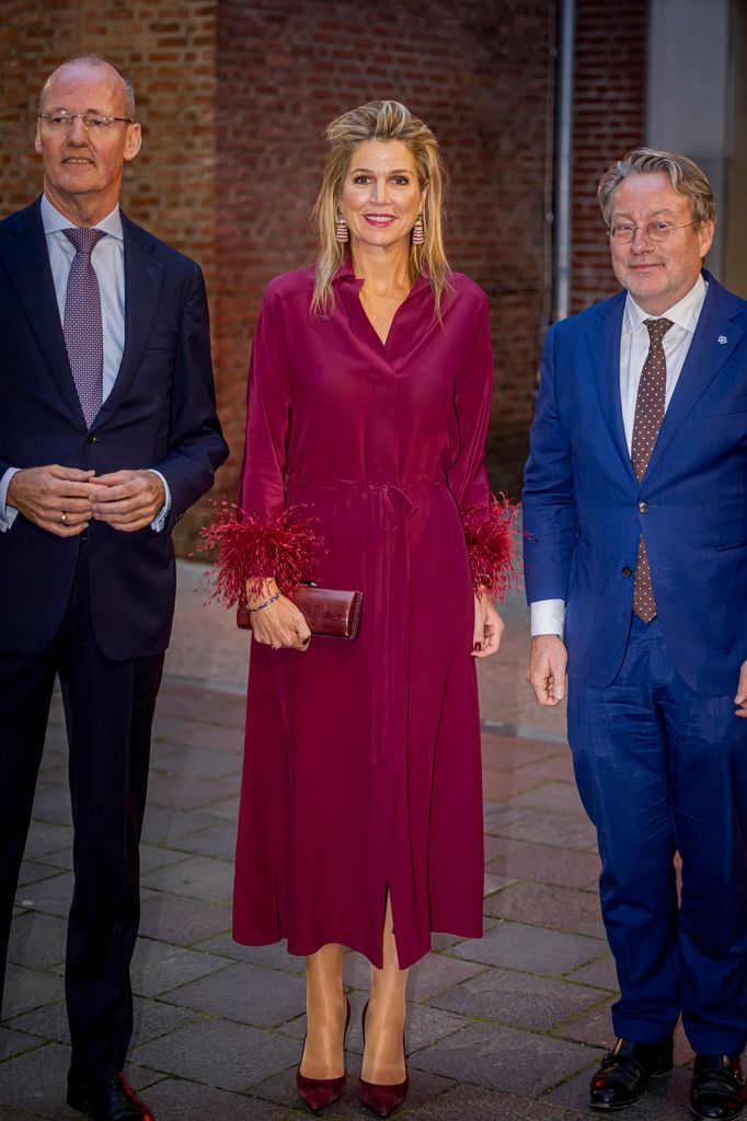 Queen Maxima in burgundy dress featuring feathered cuffs between two men