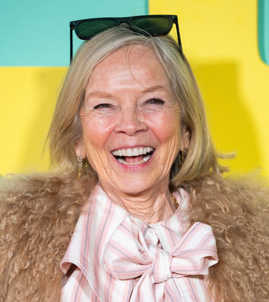 Jo Wood dans un manteau moelleux et un chemisier rayé souriant largement