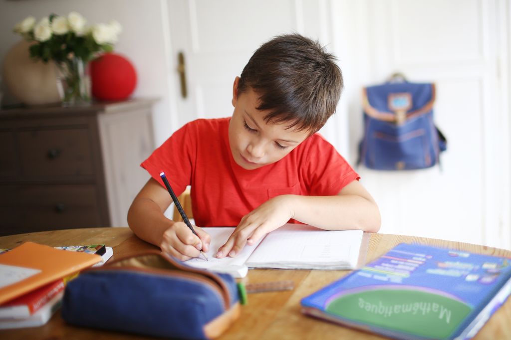 A 7 years old boy doing his homework in red t-shirt