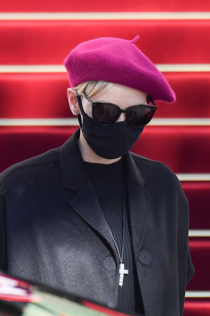 Princess Charlene in a black outfit and facemask with sunglasses and a maroon beret