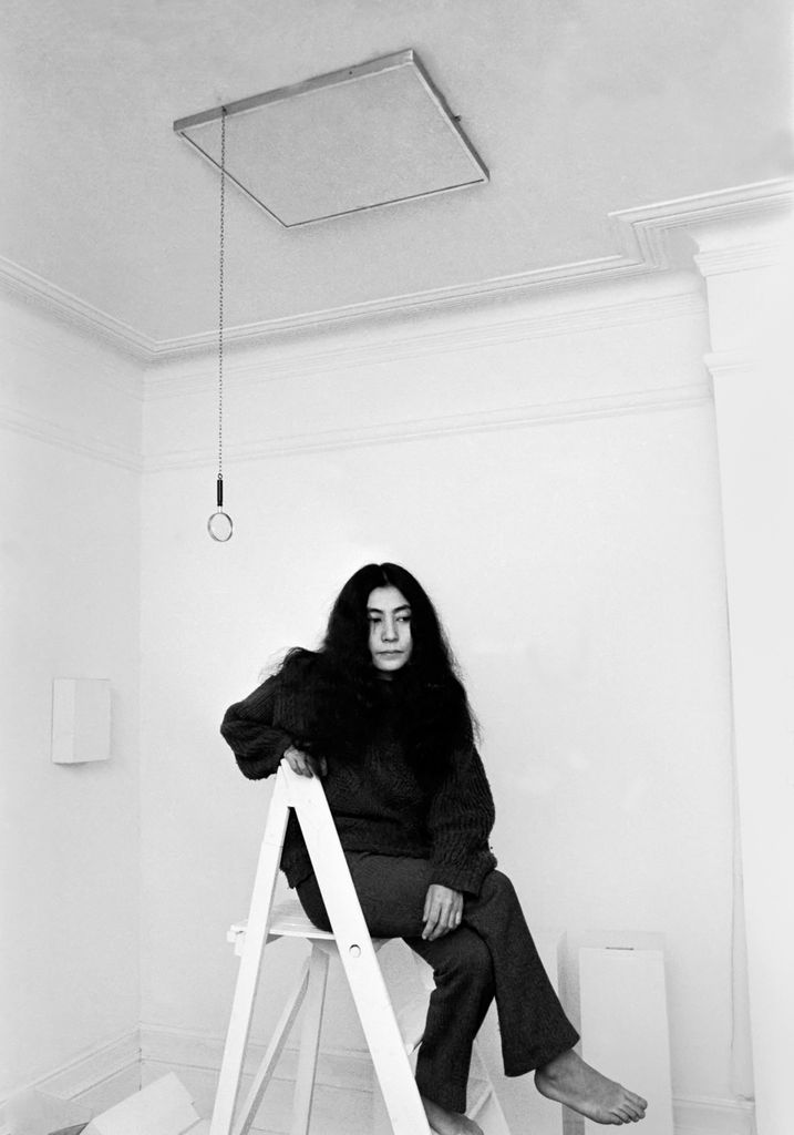 Yoko Ono est assise sur une échelle blanche.