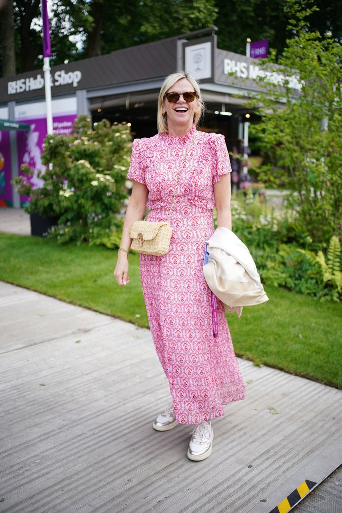 Zoe Ball wears a pink patterned midi dress with puff sleeves, white sneakers, a straw belt bag and sunglasses at the Chelsea Flower Show 2025.