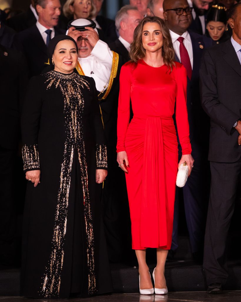 Rania in a red dress beside woman in black dress