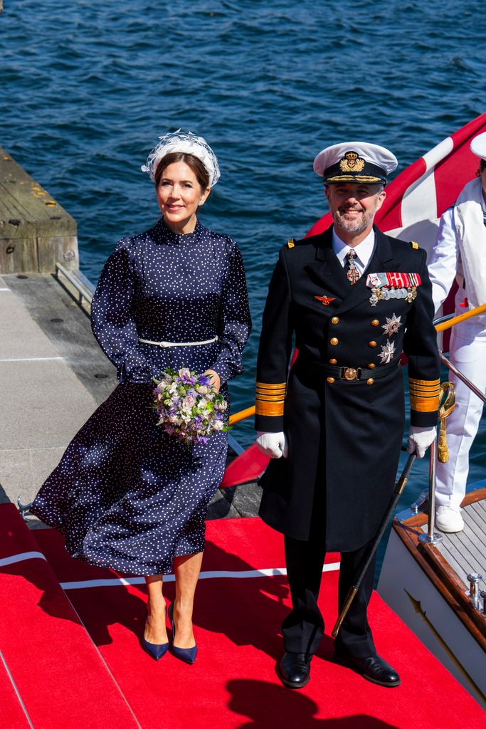 Queen Mary holding a bunch of flowers standing with King Frederik who wears a naval uniform