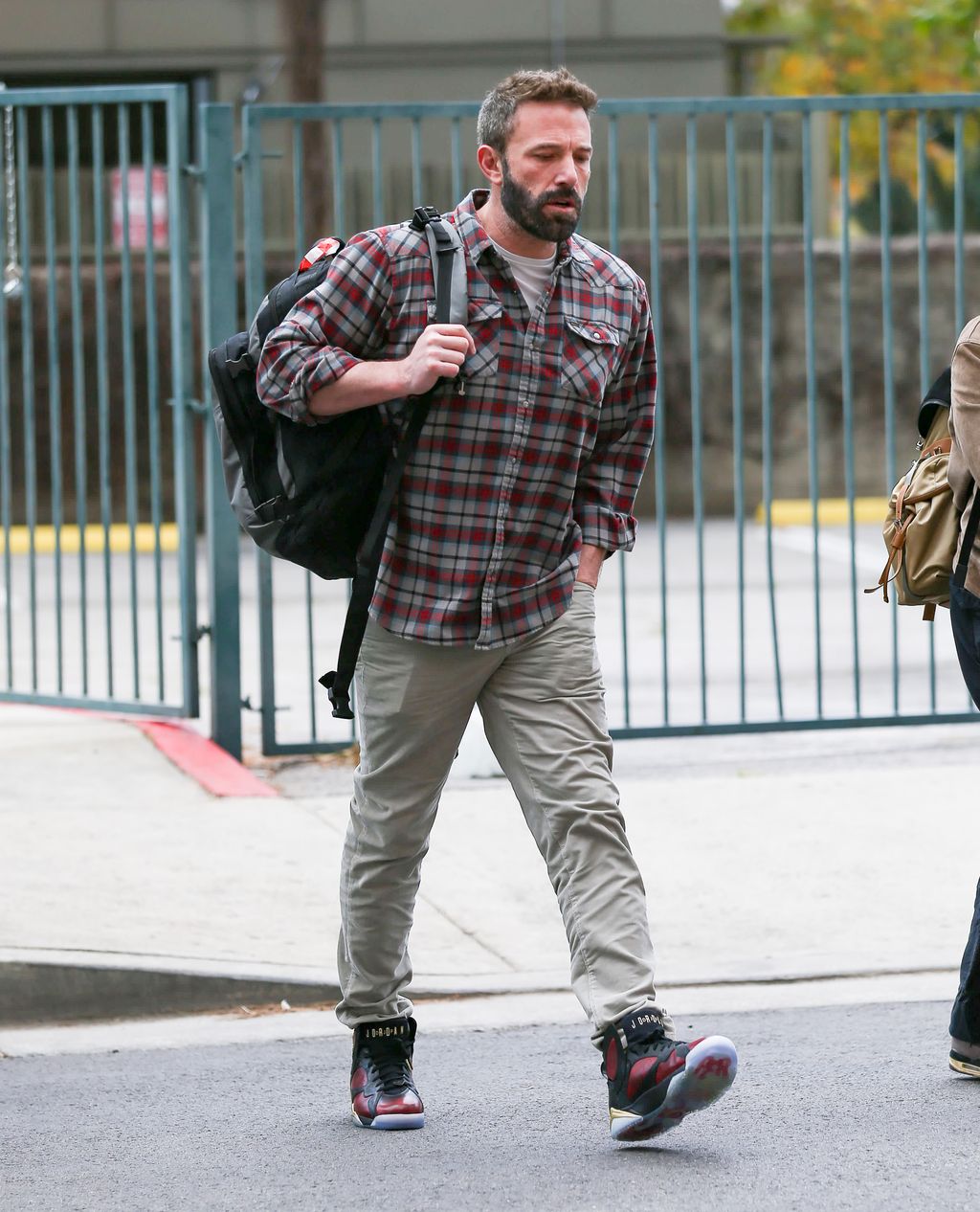 Ben Affleck sporting normcore staples, some baggy trousers, a plaid shirt, sneakers and a backpack