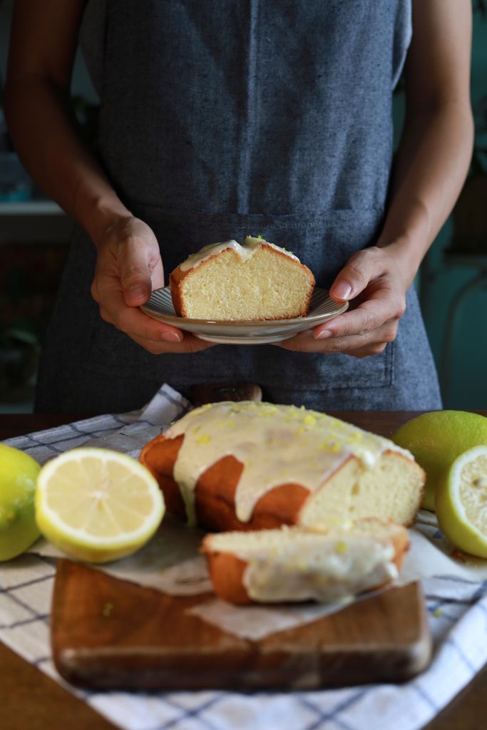 Women wearing an apron, holding a plate of freshly baked lemon cake with lemon glaze