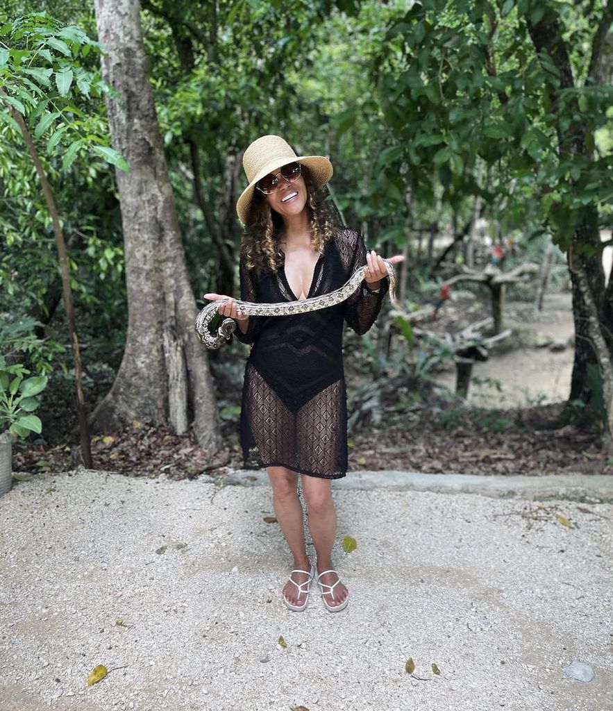 Halle Berry in a black swimsuit and coverup holding a snake skin