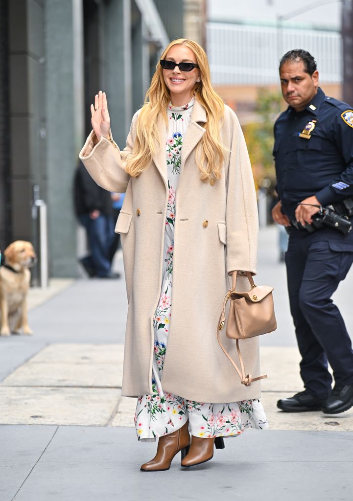 Lindsay Lohan waving on street in floral dress and cream coat