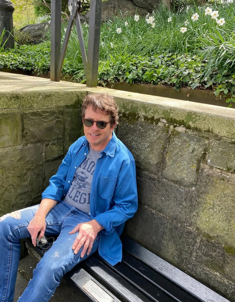 Photo shared by Tracy Pollan of Michael J. Fox on a park bench in honor of his 65th birthday, June 2025