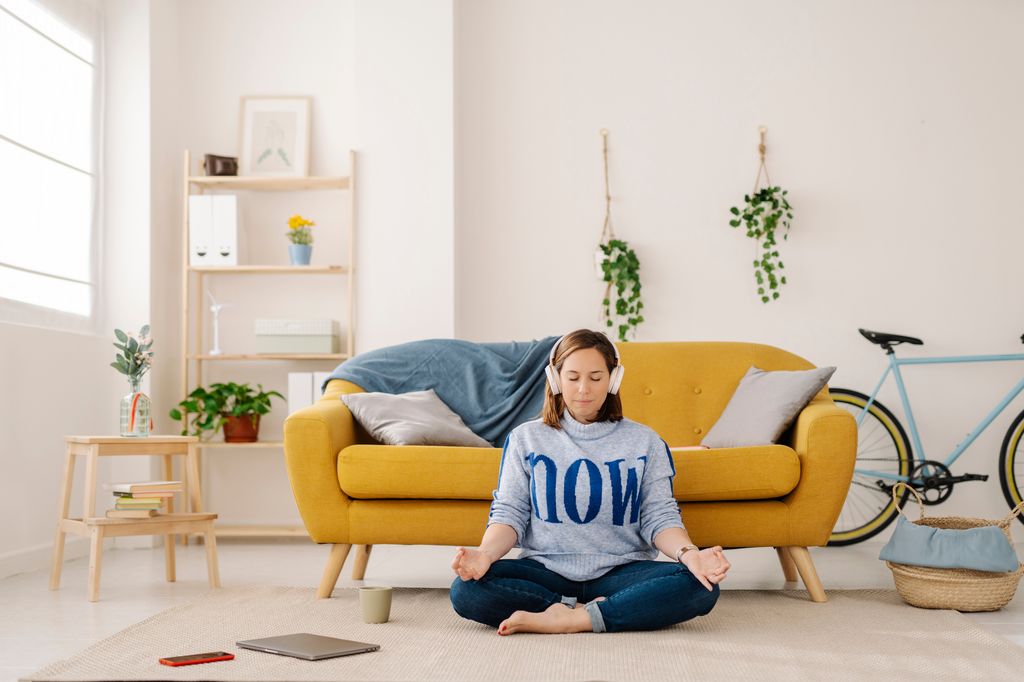 Relaxed woman using headphones while meditating during a break from work at home. Yoga and wellbeing concept.