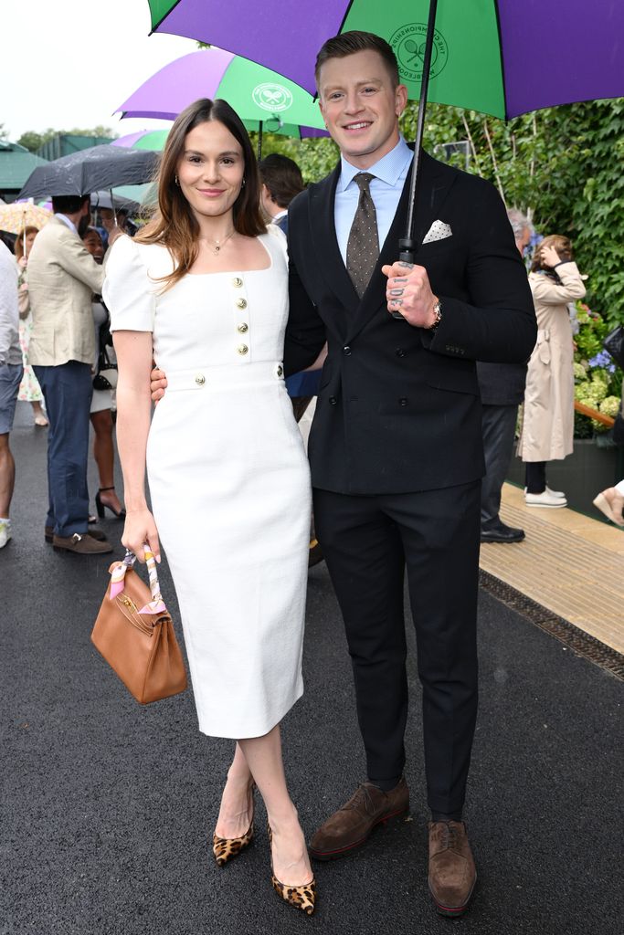 Holly Ramsay in a white dress and Adam Peaty in a black suit holding an umbrella