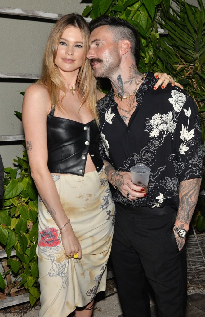 Behati Prinsloo has her arm around Adam Levine as he goes to say something to her