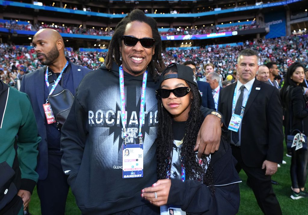 Blue Ivy with her dad at the 2023 Superbowl both are wearing sunglasses and standing in front of a large crowd