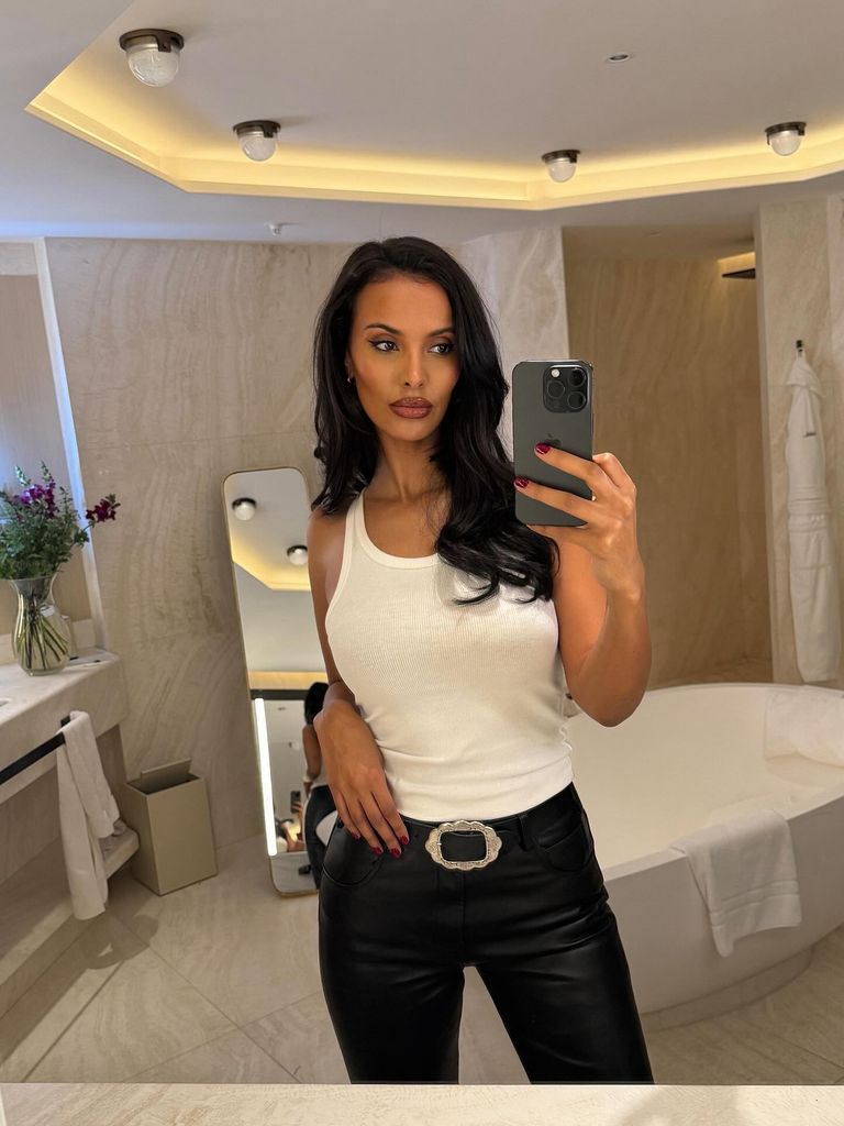 Maya Jama takes a mirror selfie in a white tank top and leather trousers. She stands in a white marble bathroom.